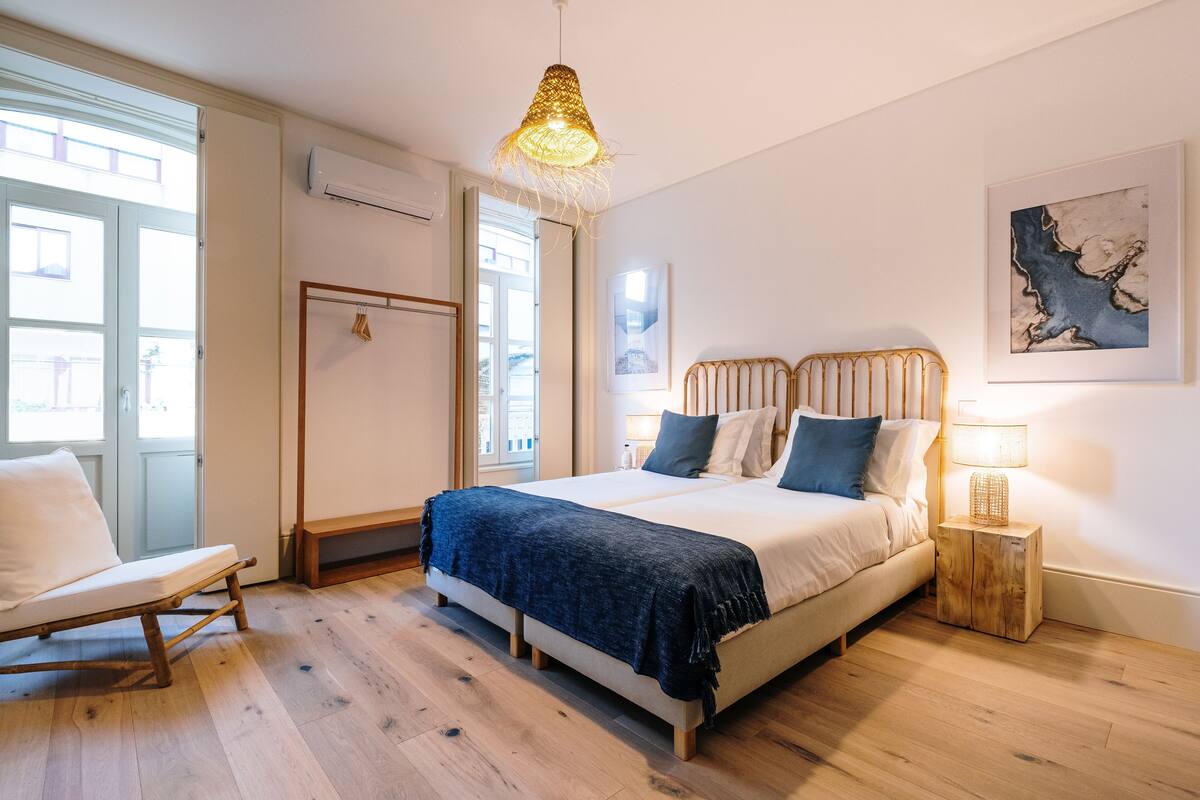 Ein Schlafzimmer mit Bett, Nachttisch, Lampe und Blick nach draußen.