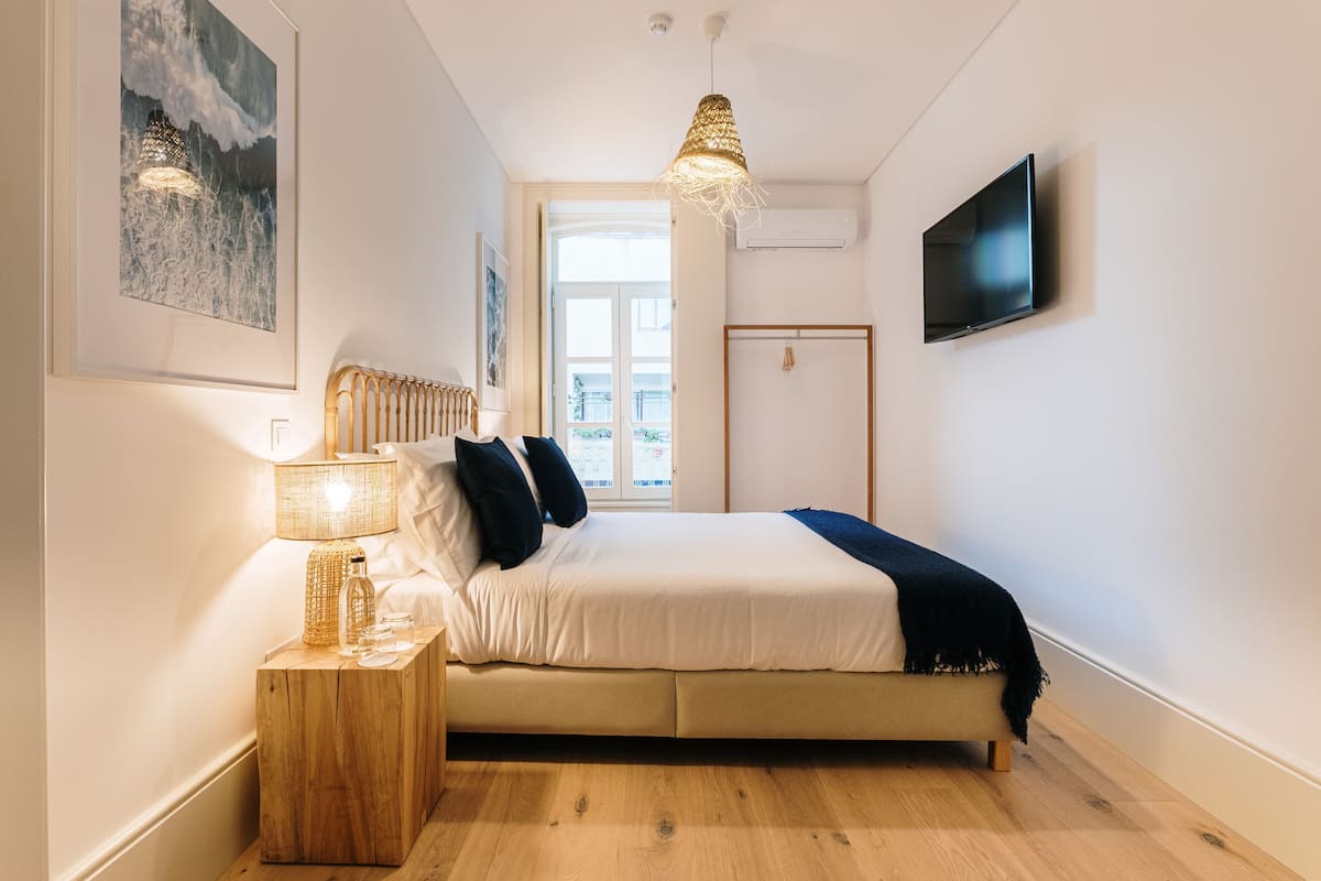 Ein Schlafzimmer mit Bett, Nachttisch, Lampe, Kunstwerk und Fernseher.