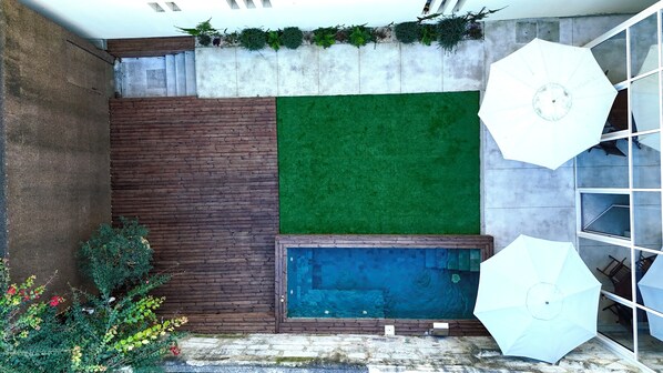 A small outdoor area with a wooden wall, a green artificial turf, a blue pool, and white umbrellas. - Ocean Porto - Beach House (Matosinhos)