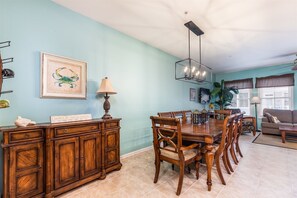 Un coin repas avec une table et des chaises en bois, un meuble avec des tiroirs, une œuvre d’art encadrée, une lampe et un luminaire au plafond.