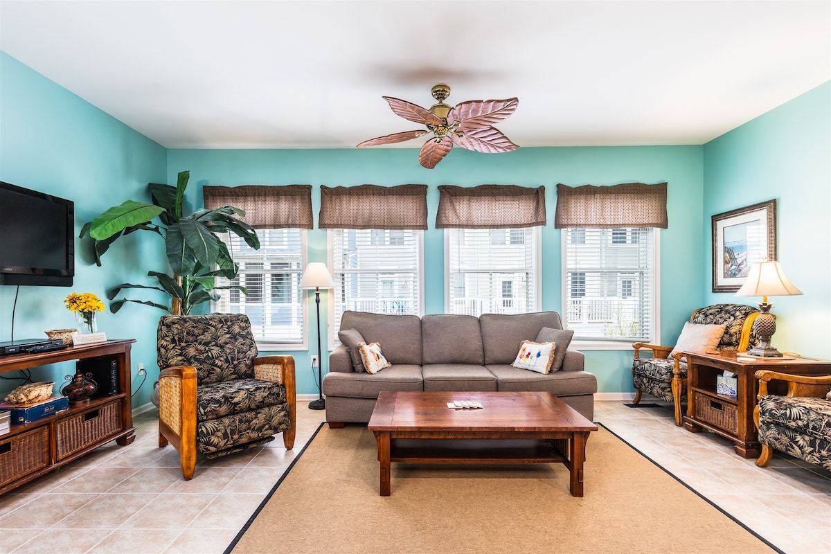 A living room with a sofa, armchairs, a coffee table, a TV, and a ceiling fan.