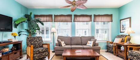 A living room with a sofa, armchairs, a coffee table, a TV, and a ceiling fan.