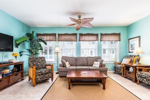 A living room with a sofa, armchairs, a coffee table, a TV, and a ceiling fan.