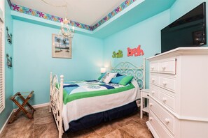 A bedroom with a bed, dresser, TV, and decorative items.