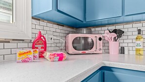 Una cocina con armarios azules, un microondas rosa y varios alimentos sobre la encimera.