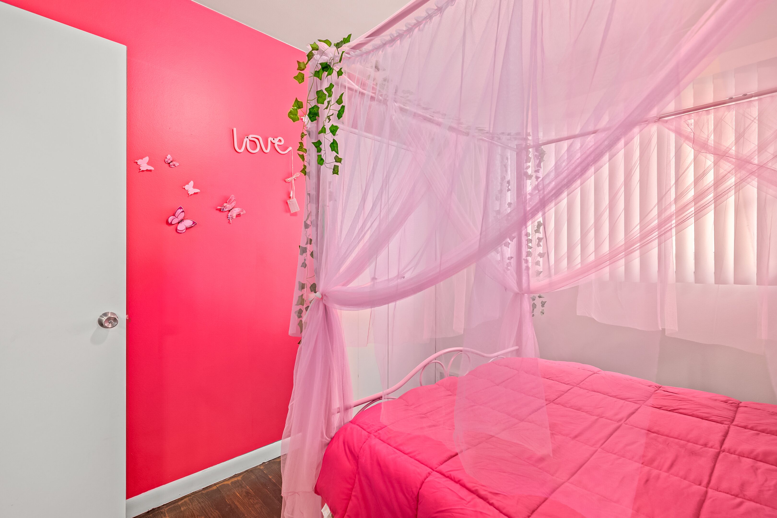Une chambre avec un lit rose, une armoire blanche et un mur rose orné du mot « amour » et de motifs de papillons.