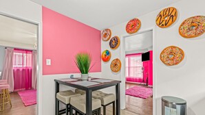 Una habitación moderna con una pared de acento rosa, un comedor con una mesa pequeña y sillas, y un cubo de basura.