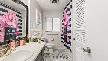 A bathroom with a white sink, toilet, and window. There are pink and black floral curtains, and a black and white patterned shower curtain.