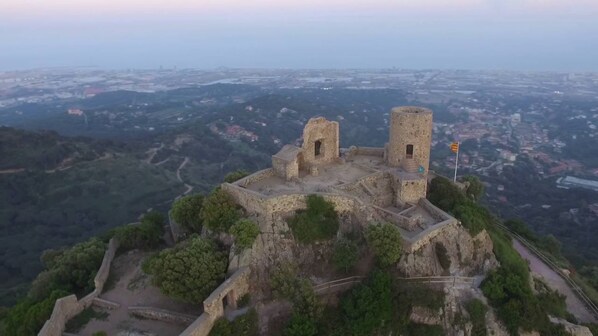 Une forteresse de pierre antique, dotée de deux tours, entourée d’une végétation luxuriante et surplombant une vallée.