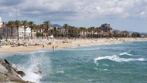 A beach with a row of palm trees, a sandy shore, and buildings in the background. - Costa Maresme 20 km BCN, Garden apartment & Private pool (Cabrils)