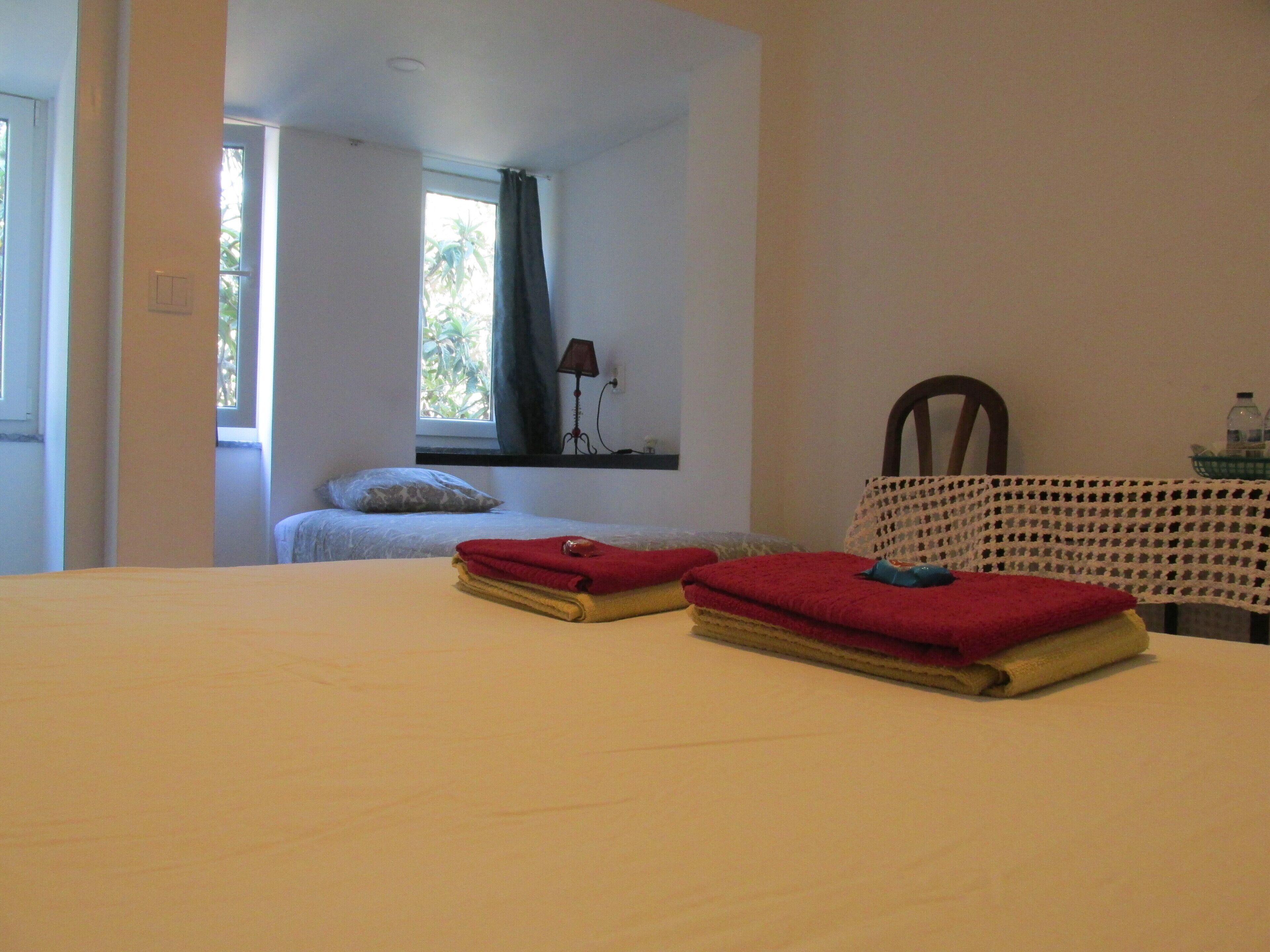 Una habitación con cama, una mesa con mantel de ganchillo y una ventana con cortinas.