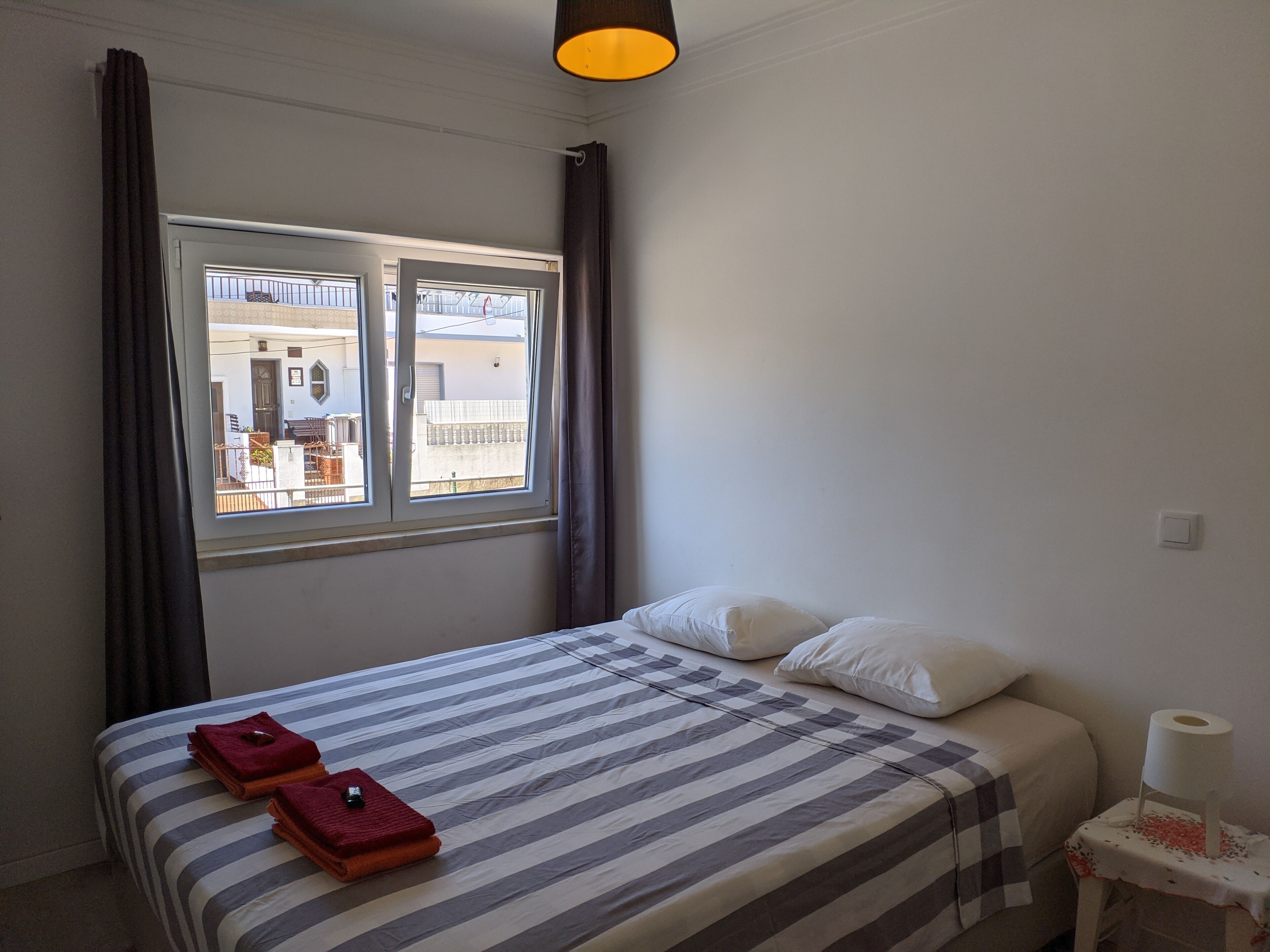 Habitación de hotel con cama, ventana, mesita de noche con lámpara y vistas al exterior.