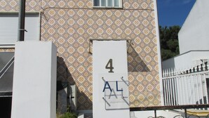 A building with a patterned facade, a white door with a number plaque, and a white fence with decorative elements. - GuestHouse Marialva Park (Seixal)