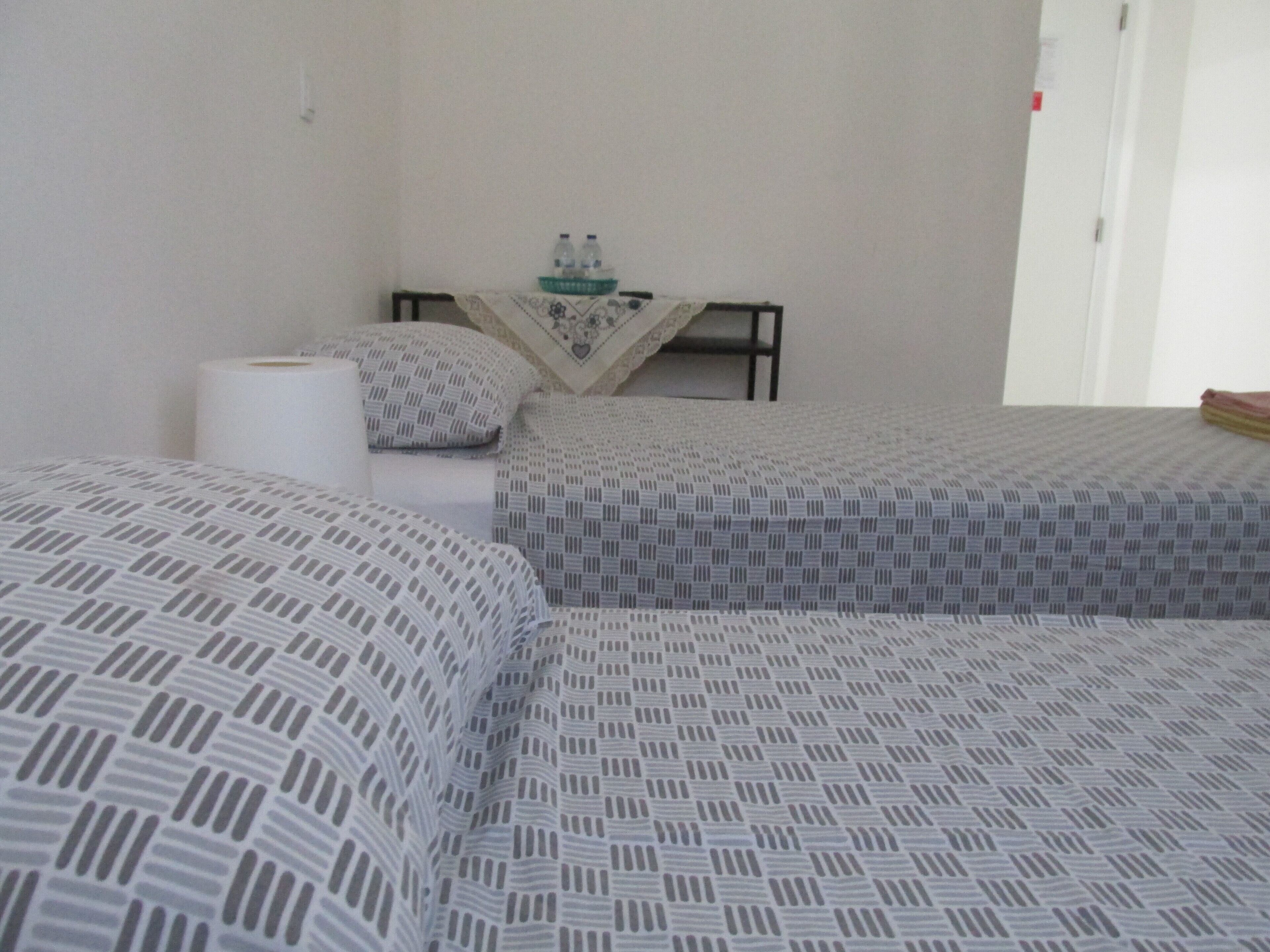 A hotel room with two beds, a table with a tablecloth, and a chair.
