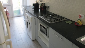 A kitchen with a gas stove, a washing machine, and a microwave. - GuestHouse Marialva Park (Seixal)