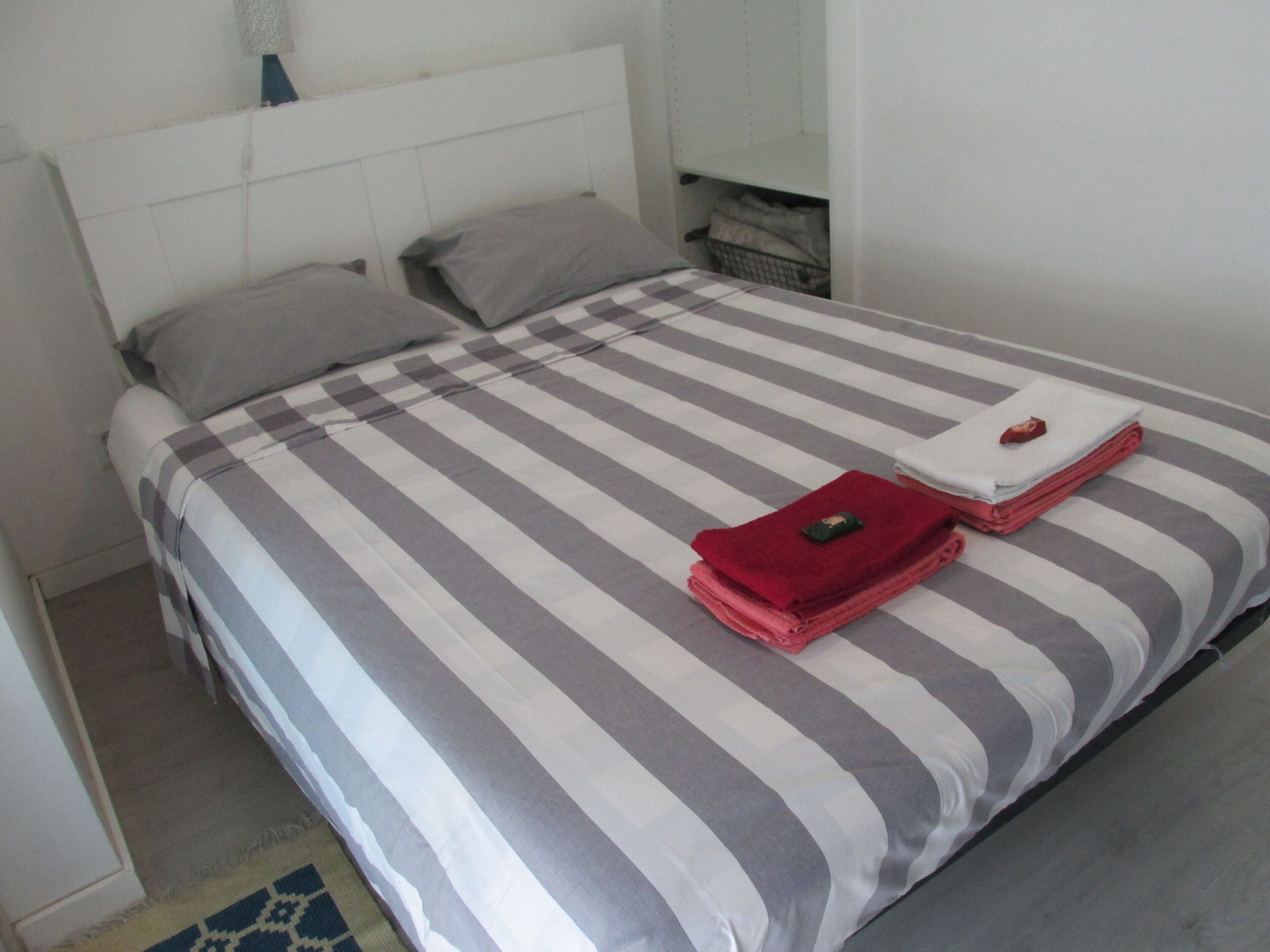 Una cama con una colcha a rayas y dos almohadas. Hay toallas dobladas sobre la cama.
