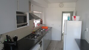 A modern kitchen with stainless steel appliances, a microwave, a gas stove, and a washing machine. - GuestHouse Marialva Park (Seixal)
