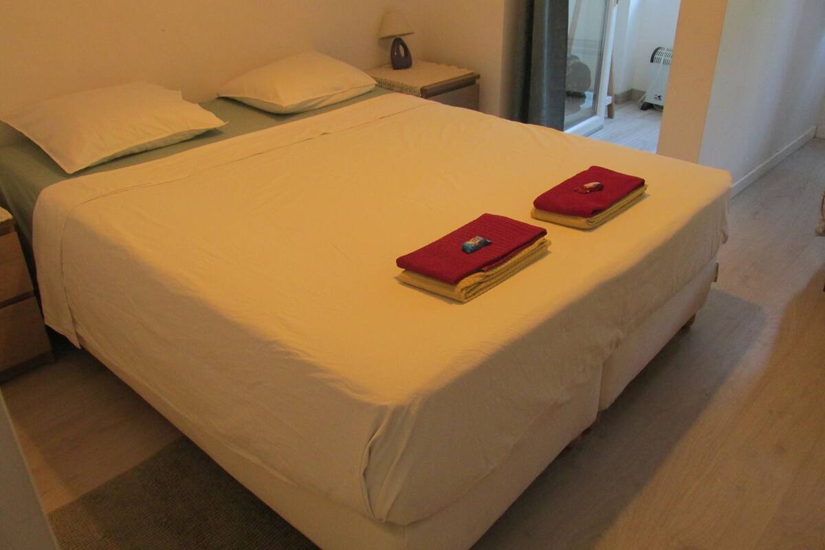 Een net opgemaakt bed met witte lakens en twee rode handdoeken er bovenop.