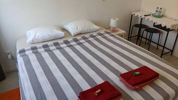 A bed with striped bedding, two pillows, a bedside table with a lamp, a basket of bottled water, and a red towel on the bed.