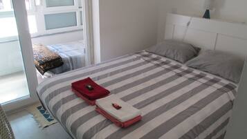 Uma cama bem arrumada com roupa de cama listrada, uma pequena mesa de cabeceira e uma janela com persianas.