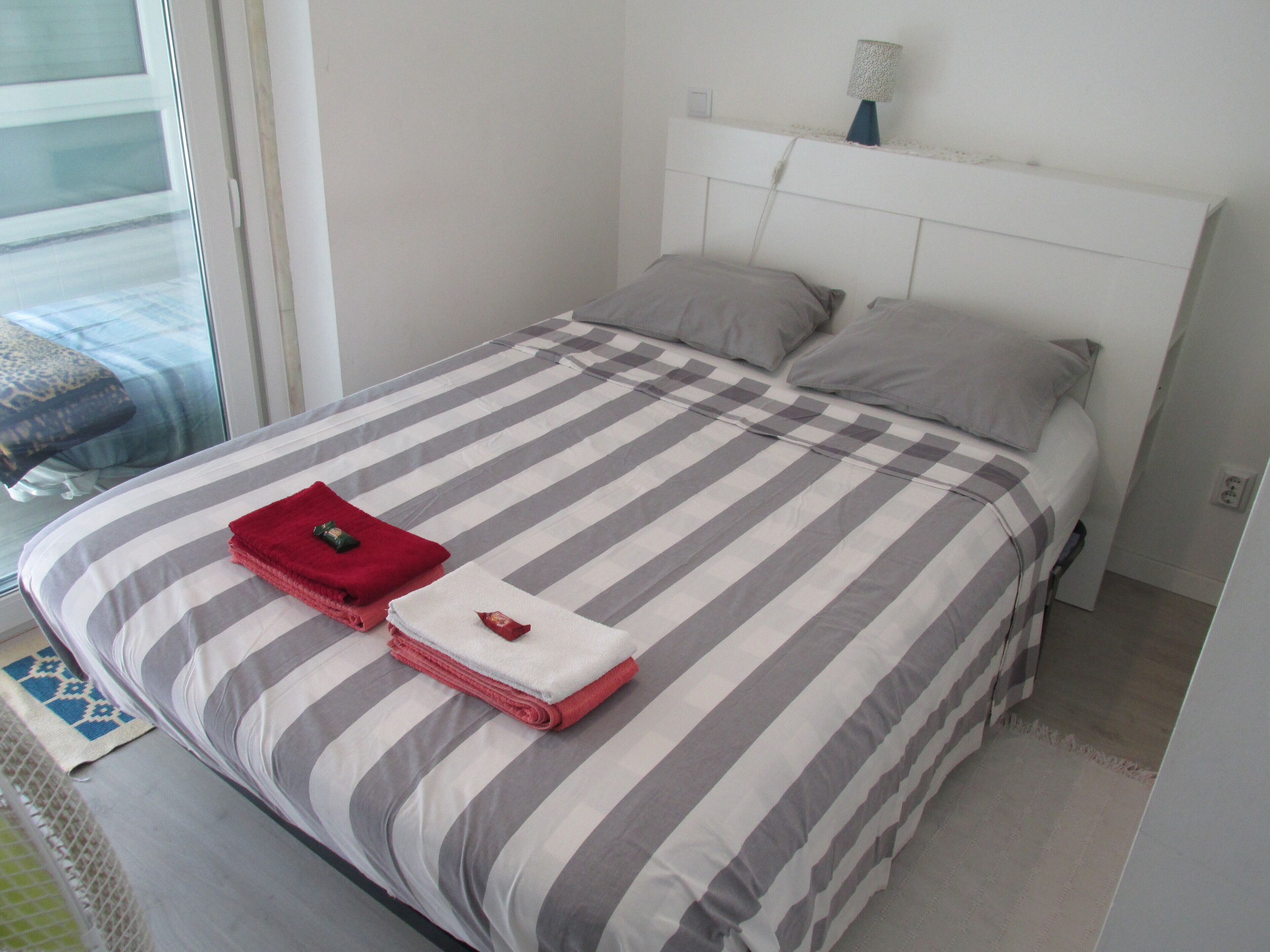 Ein Bett mit gestreifter Bettwäsche, ein rotes und weißes Handtuch sowie eine Lampe auf dem Nachttisch.