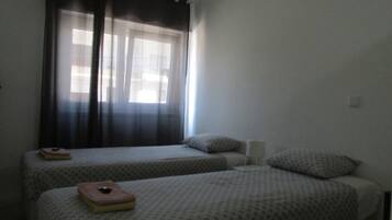 Une chambre avec deux lits simples, une fenêtre avec des rideaux et un petit tabouret.