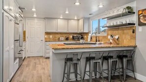 A modern kitchen with white cabinets, a granite countertop, and bar stools. - Spacious 4BR RanchHome w/2FirePits (Atascadero)
