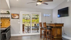 A modern kitchen with a bar area, wooden flooring, and a large sliding glass door leading to an outdoor patio. - Spacious 4BR RanchHome w/2FirePits (Atascadero)