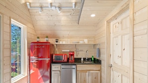 Cocina compacta con paredes de madera, un refrigerador rojo, un microondas, una cafetera y un lavavajillas.