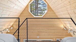 Interior de madera con un tragaluz hexagonal, una escalera y vistas a árboles.