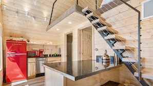 Una cocina moderna con paredes de madera, un refrigerador rojo, un lavamanos de acero inoxidable y una isla con encimera de vidrio.