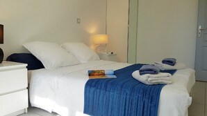 A neatly made bed with white bedding and a blue throw blanket, a bedside table with a lamp, and a door in the background. - 200m from the ocean, villa "Lupin" in residence with swimming pool . : Les Thalassiles (Fouras)