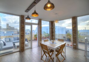 A spacious balcony with a dining area, large windows, and a city view.