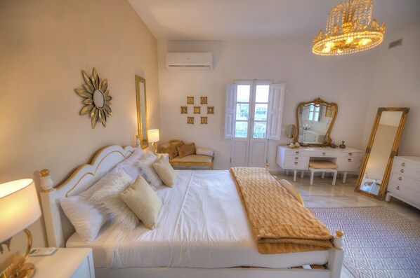 A bedroom with a large bed, bedside tables, a dresser, a vanity with a mirror, and a chandelier.