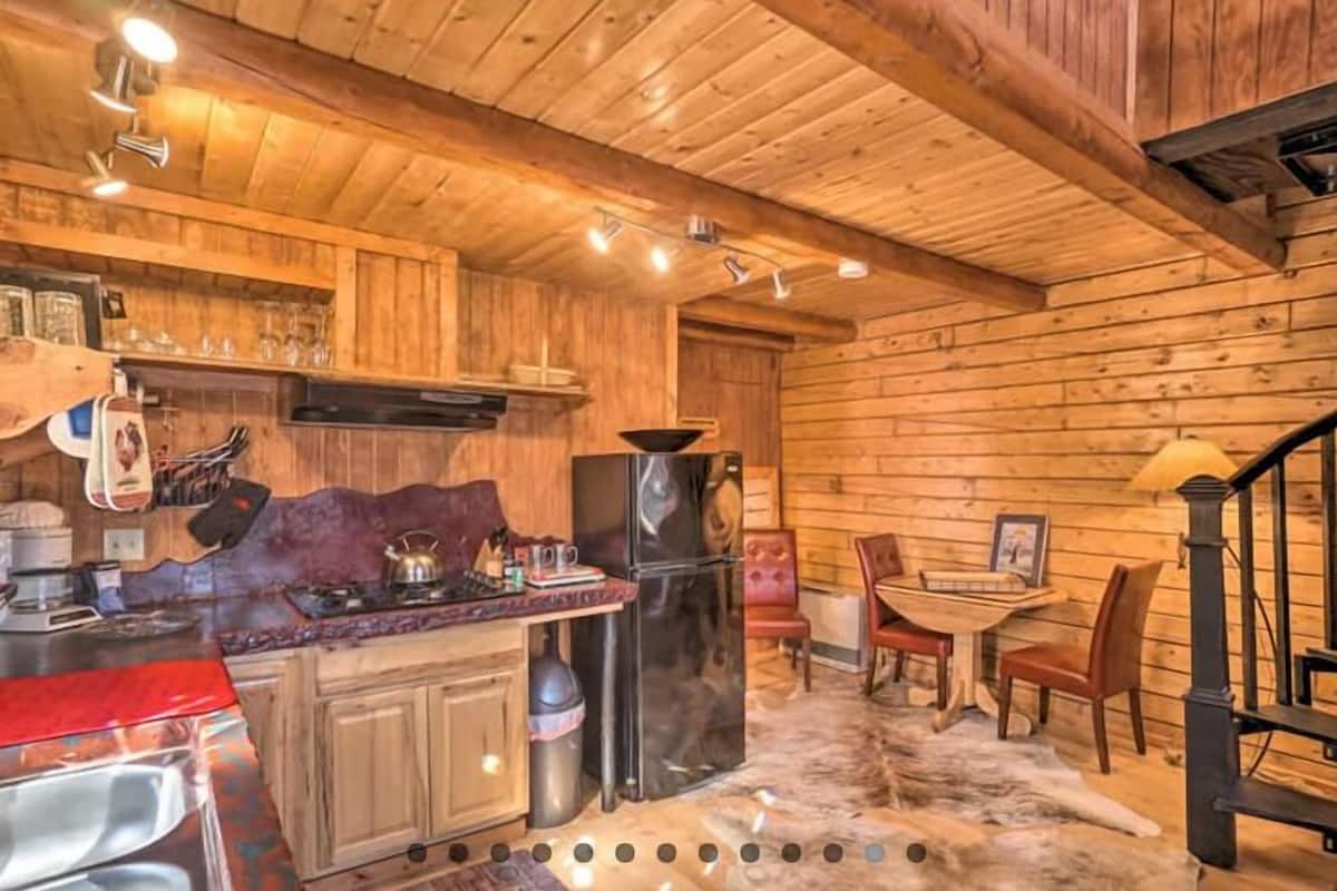 Interior de una cabaña de madera con cocina, comedor y escalera.