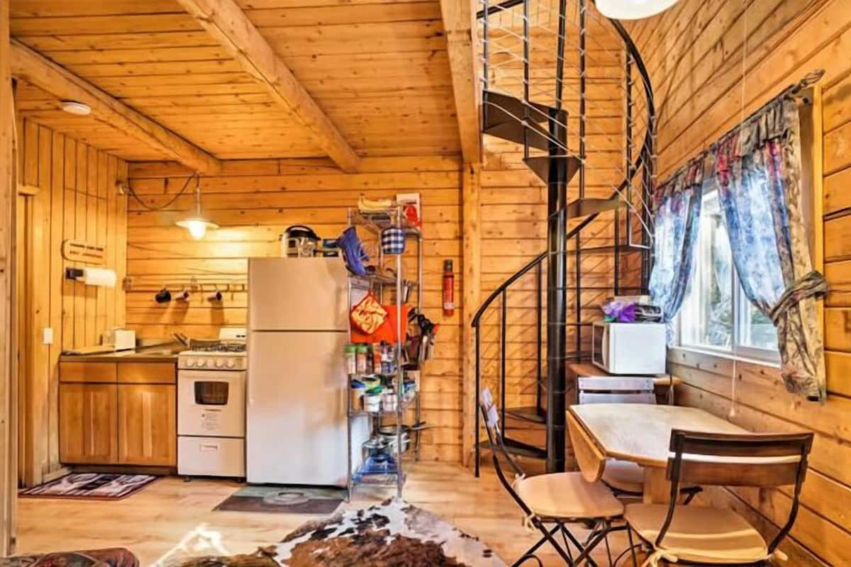 Interior de una cabaña de madera con cocina, comedor y escalera en espiral.