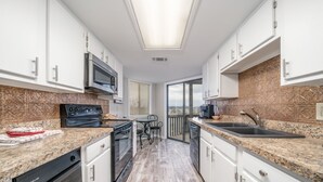 Eine moderne Küche mit weißen Schränken, Granit Arbeitsplatten, einem eingebauten Backofen, einer Mikrowelle und einem Geschirrspüler.