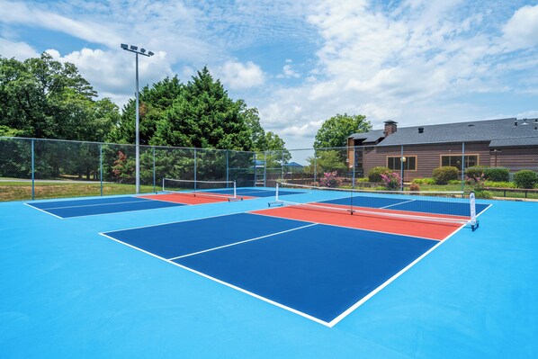 A tennis court with a net, surrounded by a fence and trees.