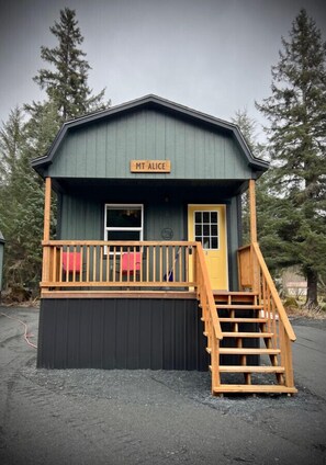 A small cabin with a wooden deck and a staircase leading to the entrance. - Mt. Alice Cozy cabin #2 of #3 built new in 2023. (Seward)