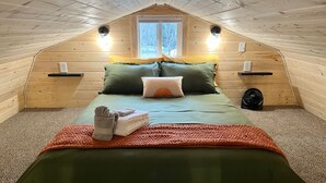 A cozy attic bedroom with a sloped ceiling, a bed with green bedding, two pillows, a fan, and a window. - Mt. Alice Cozy cabin #2 of #3 built new in 2023. (Seward)
