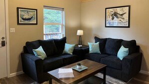 A living room with two dark sofas, a coffee table, a lamp, and two framed pictures on the walls. - Mt. Alice Cozy cabin #2 of #3 built new in 2023. (Seward)