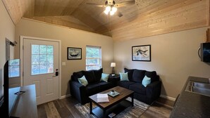 A cozy living room with a ceiling fan, two couches, a coffee table, and a TV. - Mt. Alice Cozy cabin #2 of #3 built new in 2023. (Seward)