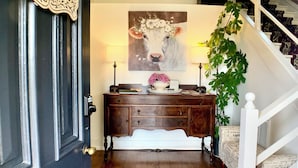 A wooden door with a 'WELCOME' sign, a wooden bench with a floral painting, a staircase, and a potted plant.