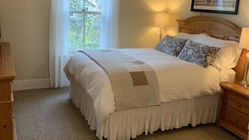 Une chambre à coucher comprenant un lit, des tables de chevet, un ventilateur de plafond, une fenêtre avec des rideaux et un tableau encadré accroché au mur.