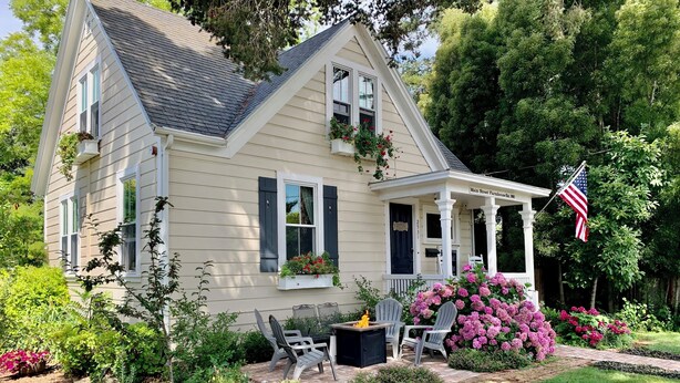 A two-story house with a porch, a small garden with flowers and a birdbath, and an American flag.