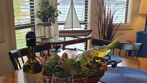 Un tavolo da pranzo con una bottiglia di vino, bicchieri, una ciotola di uva e una di frutta secca, e un tagliere di legno con formaggio.