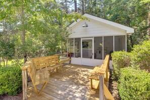 A wooden deck with benches, a covered structure with glass doors, surrounded by trees.