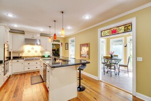 A kitchen with white cabinets, a stove, and a bar area with stools.