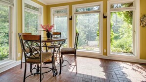Una habitación luminosa con una mesa de comedor, sillas y ventanas amplias que dan a vistas de vegetación.