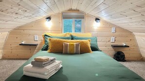 Een gezellig slaapkamer op zolder met een schuine kap, een bed met groene beddengoed, twee nachtkastjes met lampen, en een raam met uitzicht.